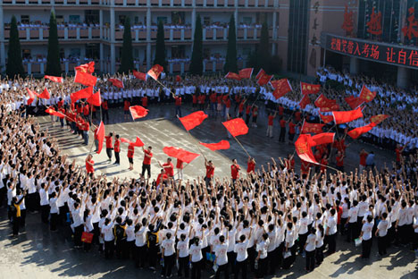 китайские студенты аплодируют учителям, машущим флагами перед началом сдачи национального вступительного экзамена